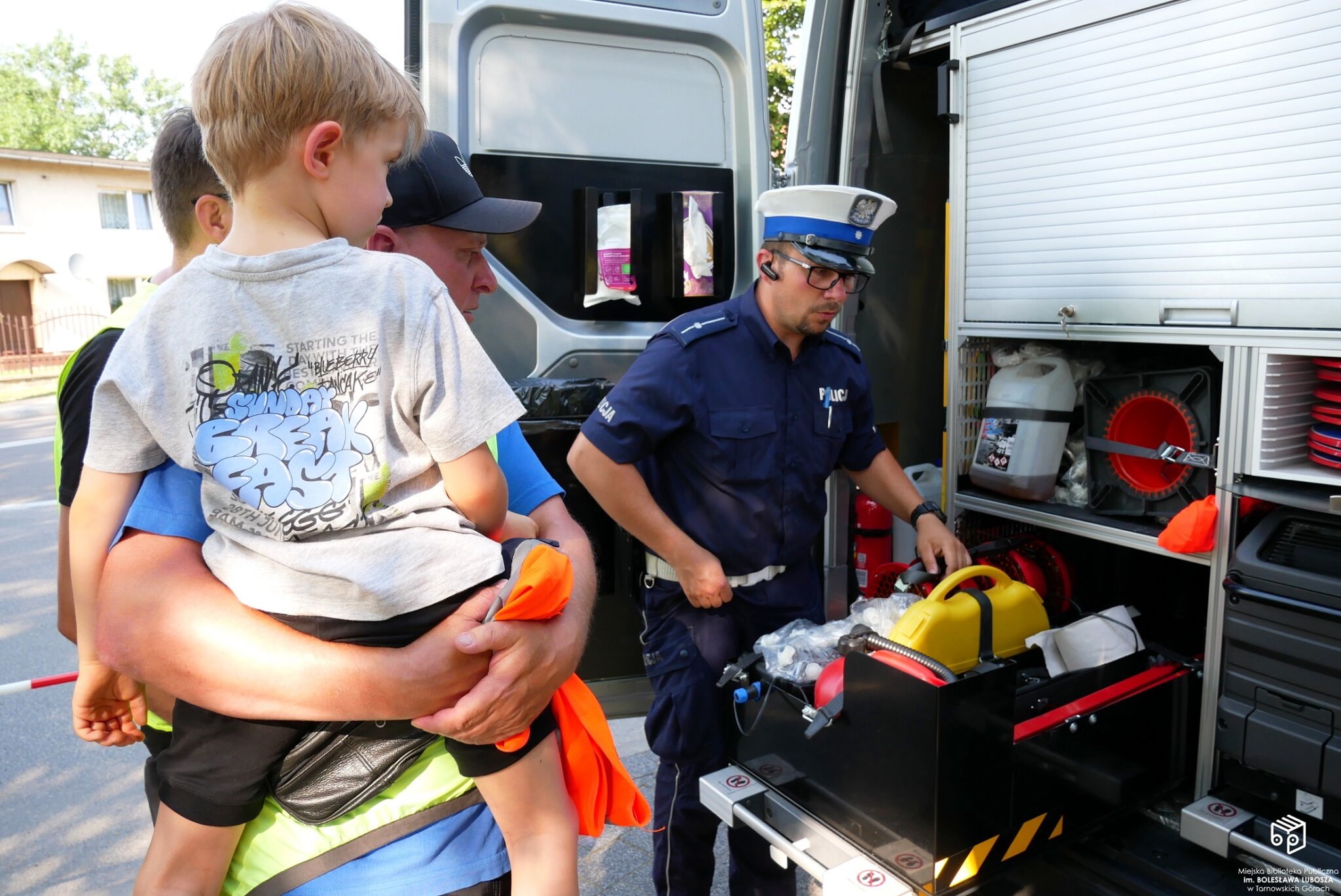 Policjanci pokazujący sprzęt z radiowozu ojcu z dzieckiem.