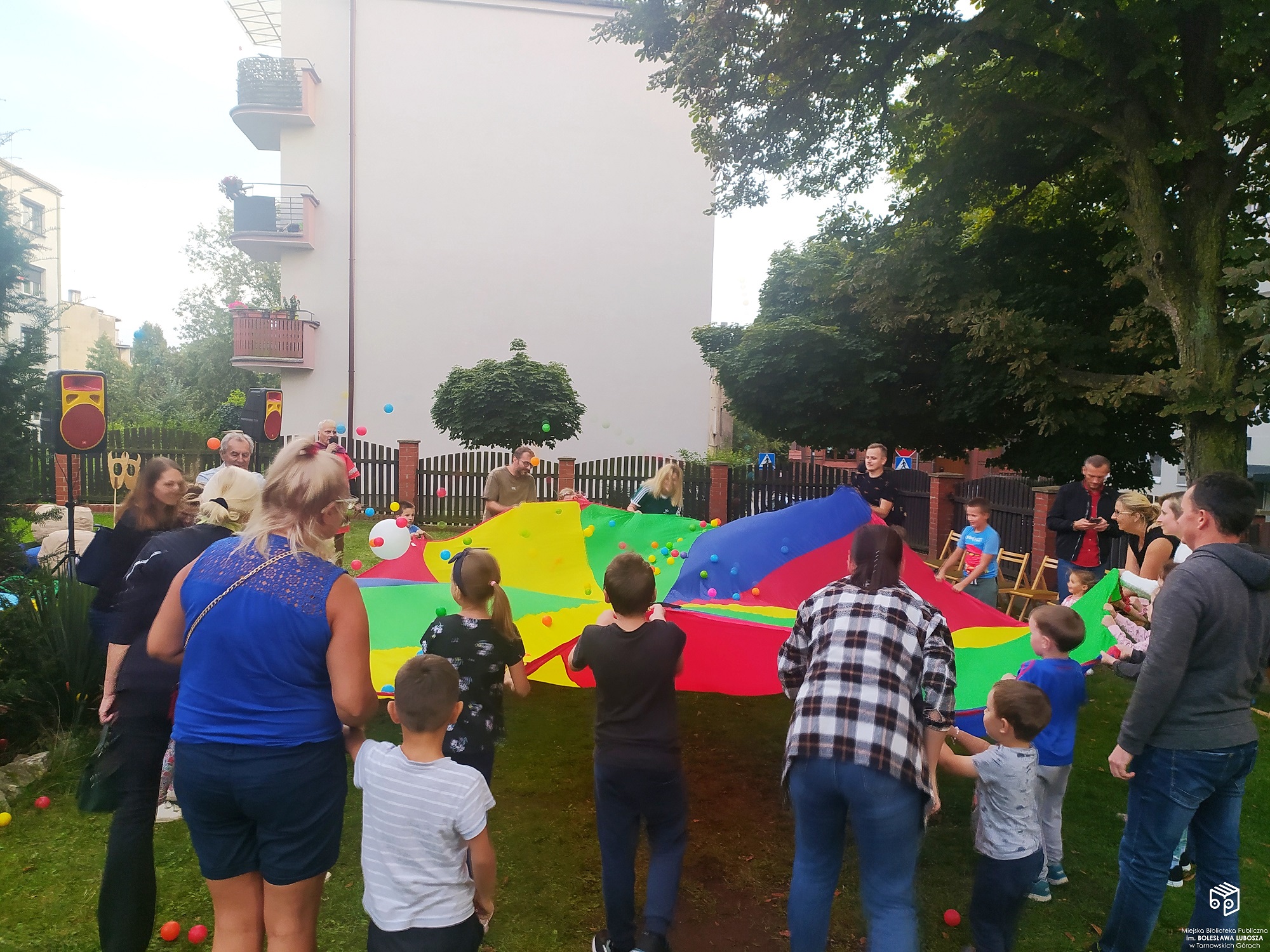 Dzieci i rodzice podrzucający kolorowe piłeczki na tęczowym materiale