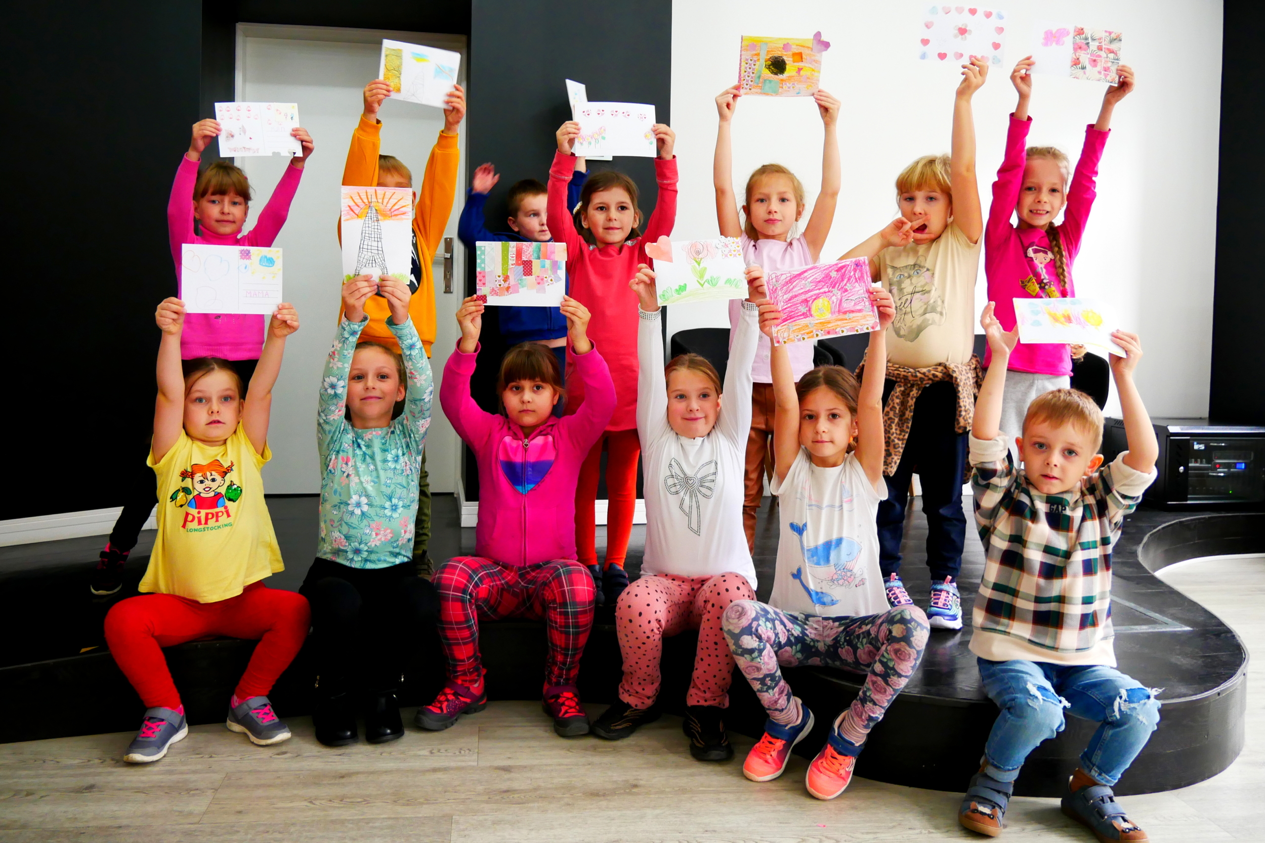 Dzieci stoją razem i pokazują narysowane pocztówki