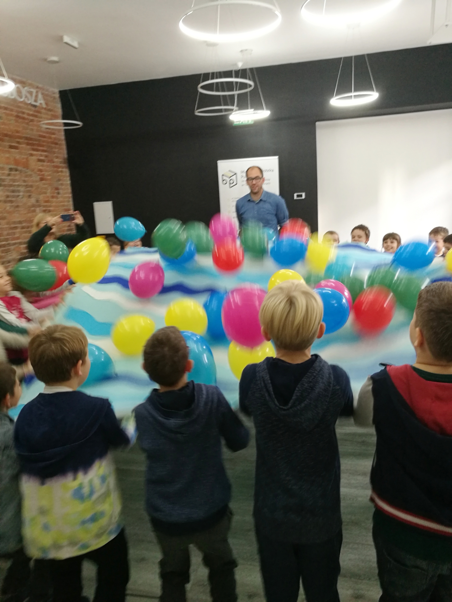 Pan Poeta bawiący się z dziećmi balonami na niebieskim materiale