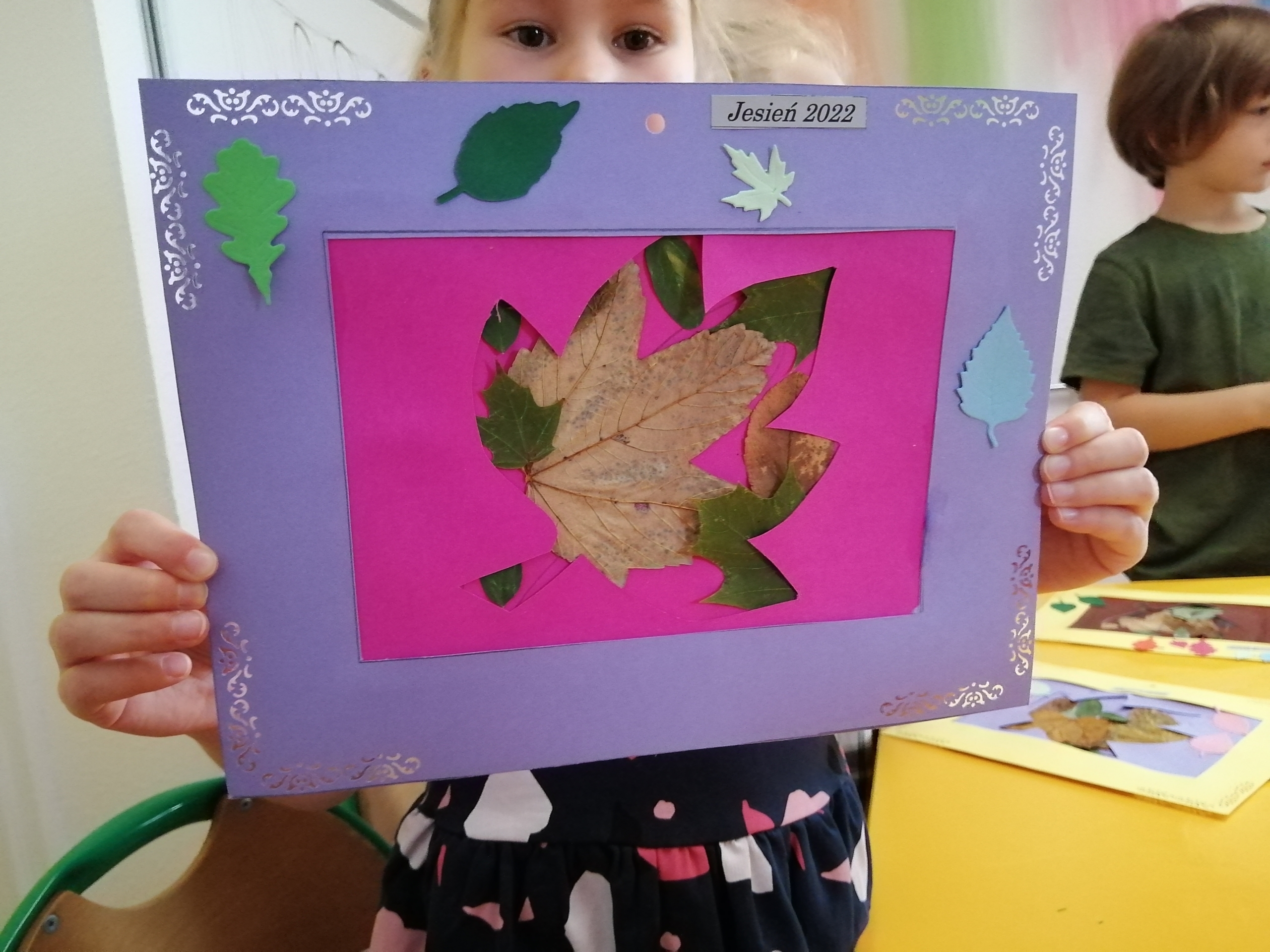 Praca plastyczna z jesiennym liściem trzymana przez dziewczynkę