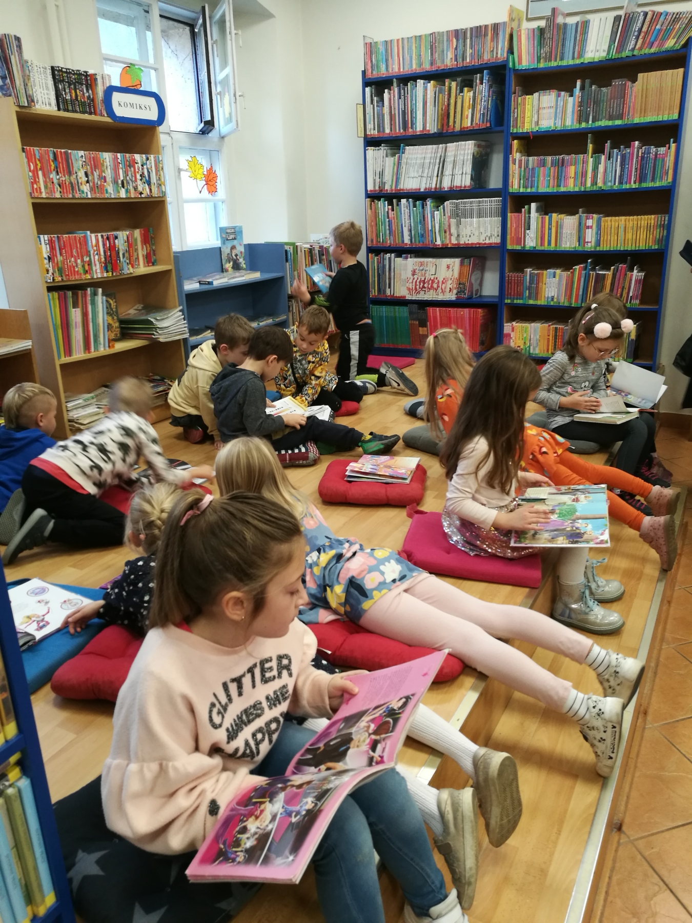 Dzieci siedząc i leżąc na podeście czytają książki