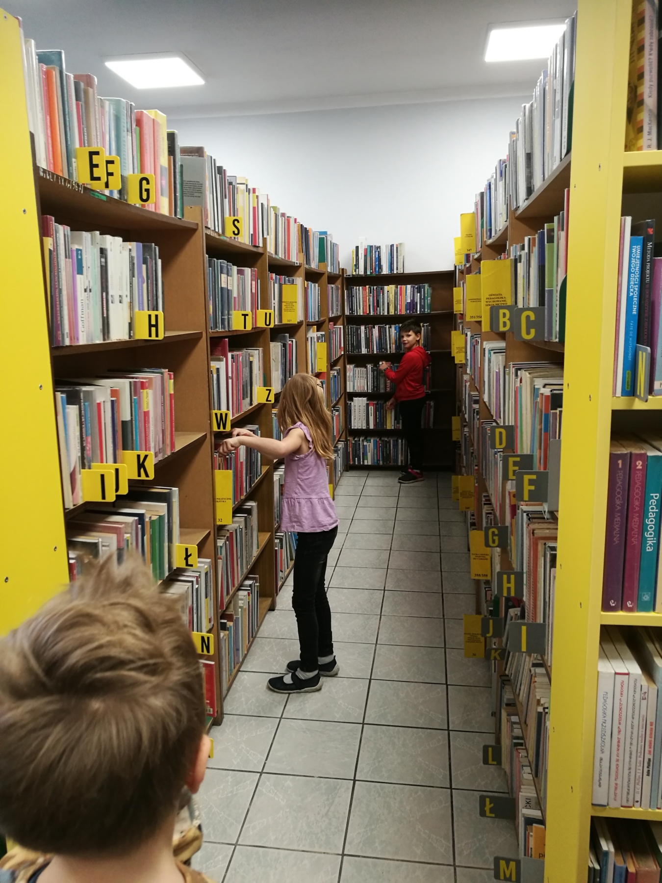 Dziewczynka oraz dwóch chłopców przeglądają książki na półce