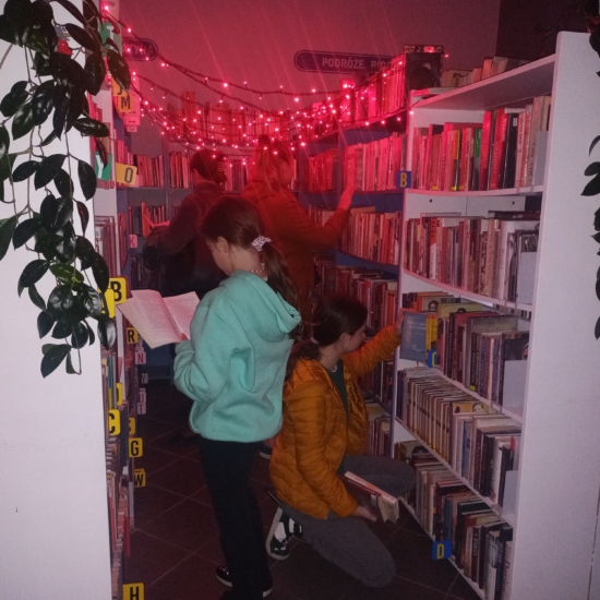 Dzieci oglądające książki przy regalach oświetlonych czerwonymi lampkami