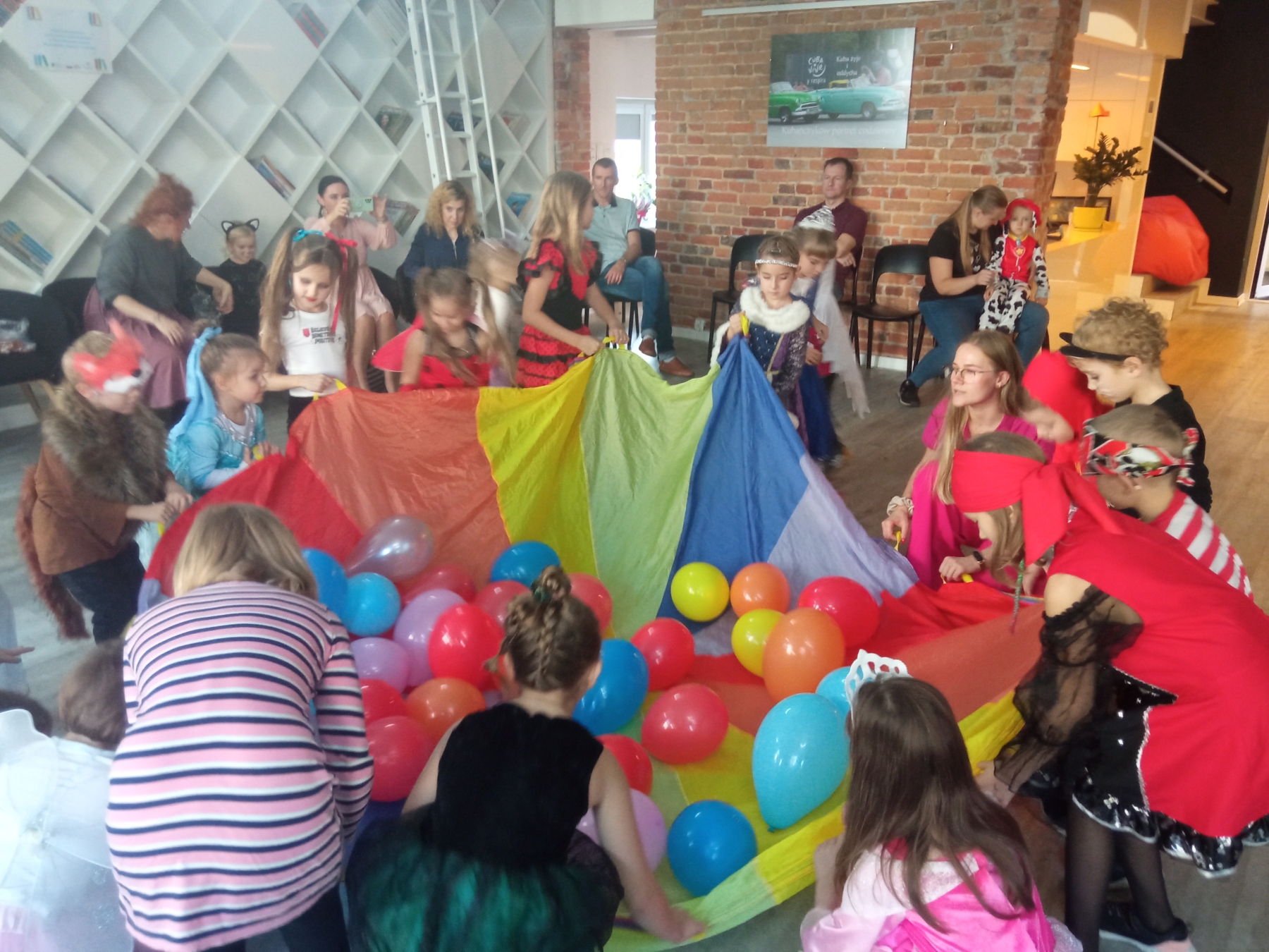 Dzieci bawią się kolorowym materiałem i balonami.