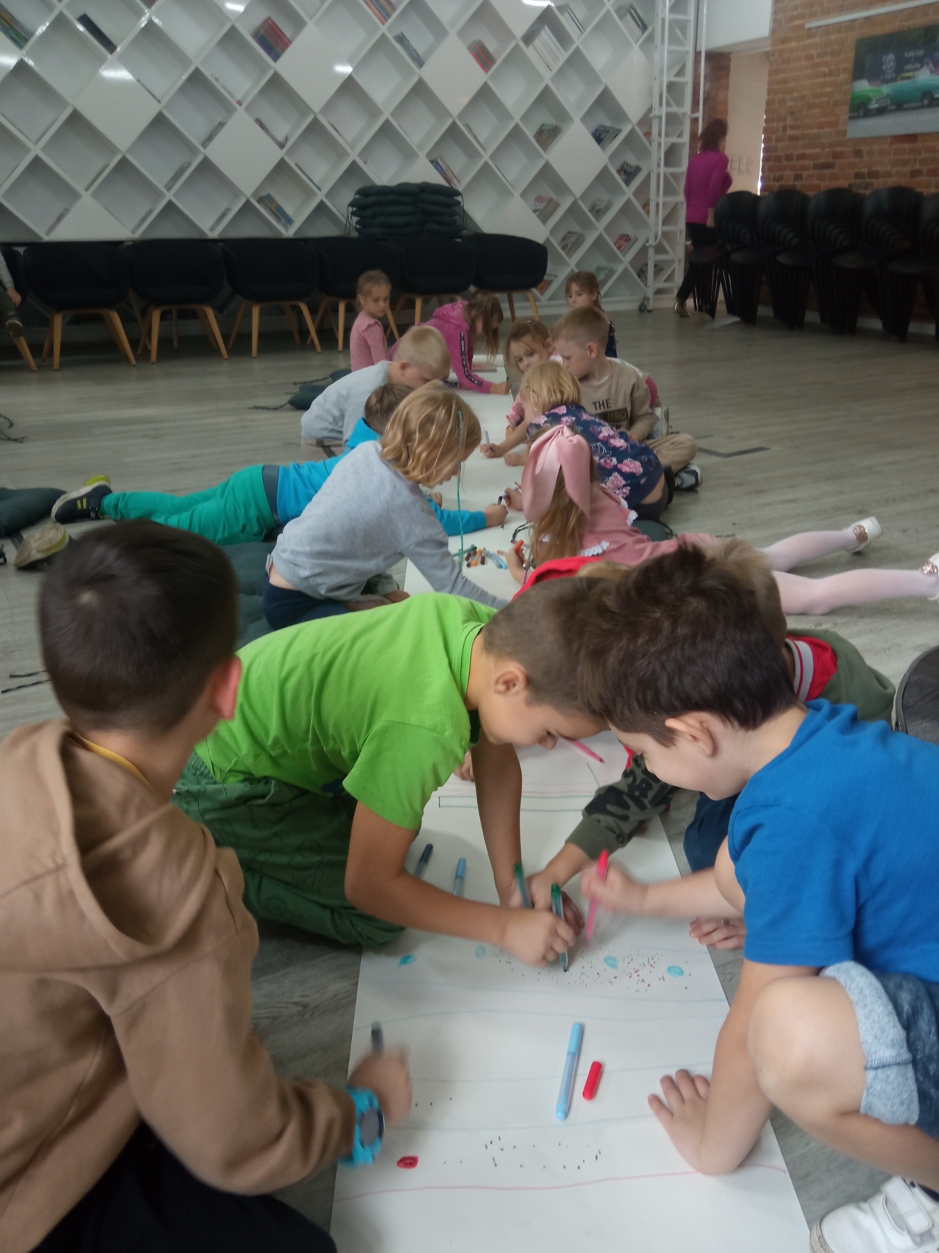 Dzieci rysują na kartkach rozłożonych na podłodze